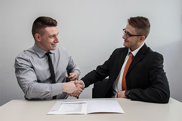 two men in suits shaking hands at a table.