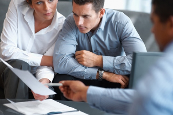 a man and woman sitting at a table looking at paperwork.