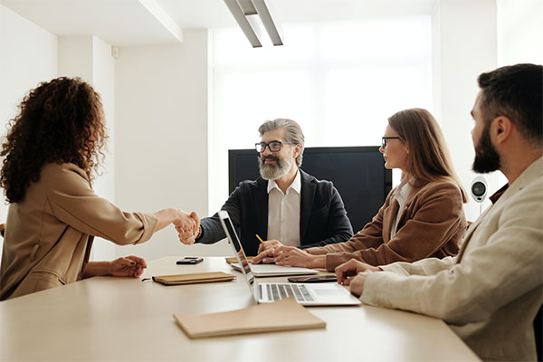 a group of people sitting around a table shaking hands.