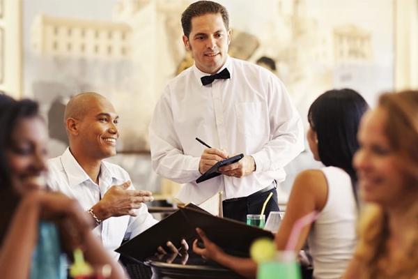 a man in a bow tie standing in front of a group of people.